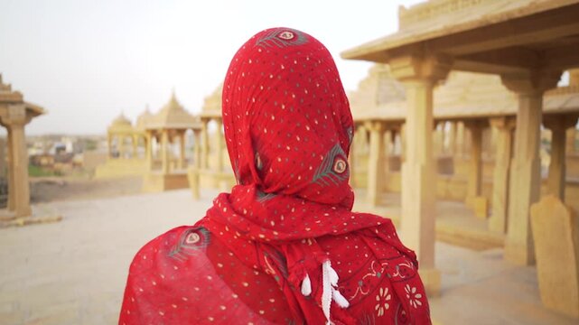 A woman in a saree moves slowly and mysteriously through the sandstone cenotaphs of Bada Bagh, Jaisalmer, India, creating an atmospheric and cinematic scene.