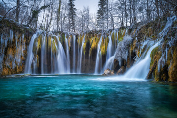 Winter waterfall, lake, frozen trees with icicles in cold evening
