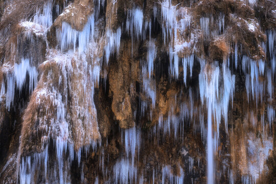 Winter frozen waterfall with icicles on moss-covered rocks - Powered by Adobe