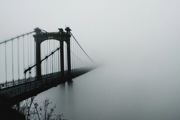 Puente colgante desapareciendo en la densa niebla sobre un río, creando una atmósfera misteriosa y surrealista