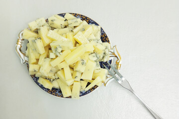 Blue cheese on a decorative serving blue plate with gold handles and a fork. White background.