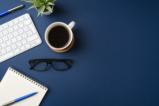 Workspace with keyboard, laptop, office supplies, pen, green leaf and coffee cup. Flat lay, top view blue office desk