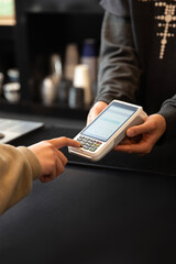Customer's hand entering PIN code on a POS payment terminal held by a cashier, completing a...