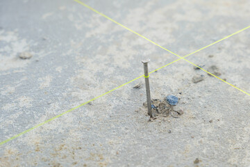 Close-up of a nail embedded in rough concrete, yellow lines intersecting at its base, demonstrating accuracy in construction and alignment for tiling projects.