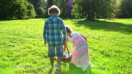 Children joyfully participate in an Easter egg hunt in a sunny park. They gather colorful eggs into a wicker basket and walk barefoot on lush grass, enjoying a cheerful spring celebration.