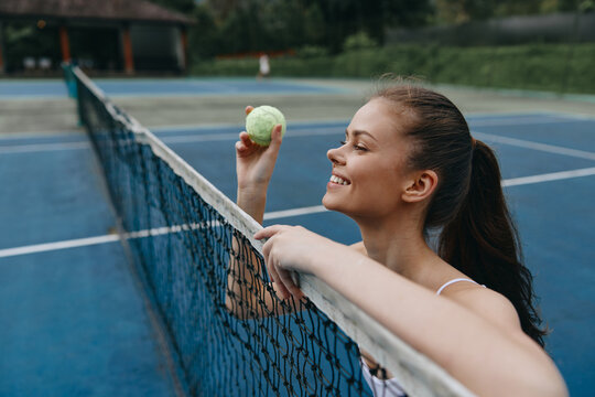 Young female tennis player smiling while holding a tennis ball on a blue court, showcasing a vibrant and energetic atmosphere perfect for sports promotion