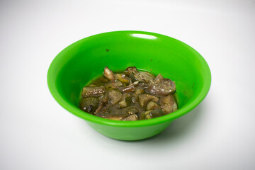 A green plastic bowl contains green eggplant vegetable dishes. The background is white.