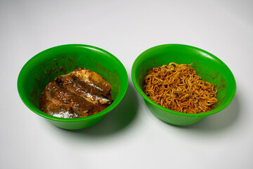 Green plastic bowl filled with sardines and fried noodles. The background is white.