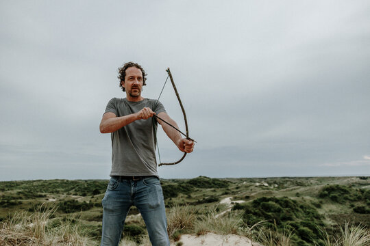 Man holding a handmade bow and arrow in a natural landscape.