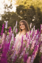 beautiful girl stands among flowers in nature in the middle of a blooming field