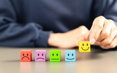 Customer satisfaction feedback survey concept. Person selects yellow smile face block from row of...