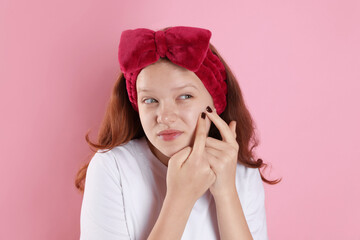 Teenage girl popping pimple on her face against pink background. Acne problem