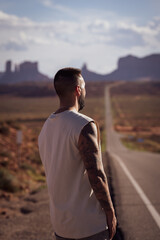 Unrecognizable young man sightseeing on the road against the backdrop of Monument Valley, on the west coast of the United States.
