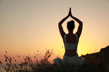 Woman meditating outdoors at sunset, back view. Space for text
