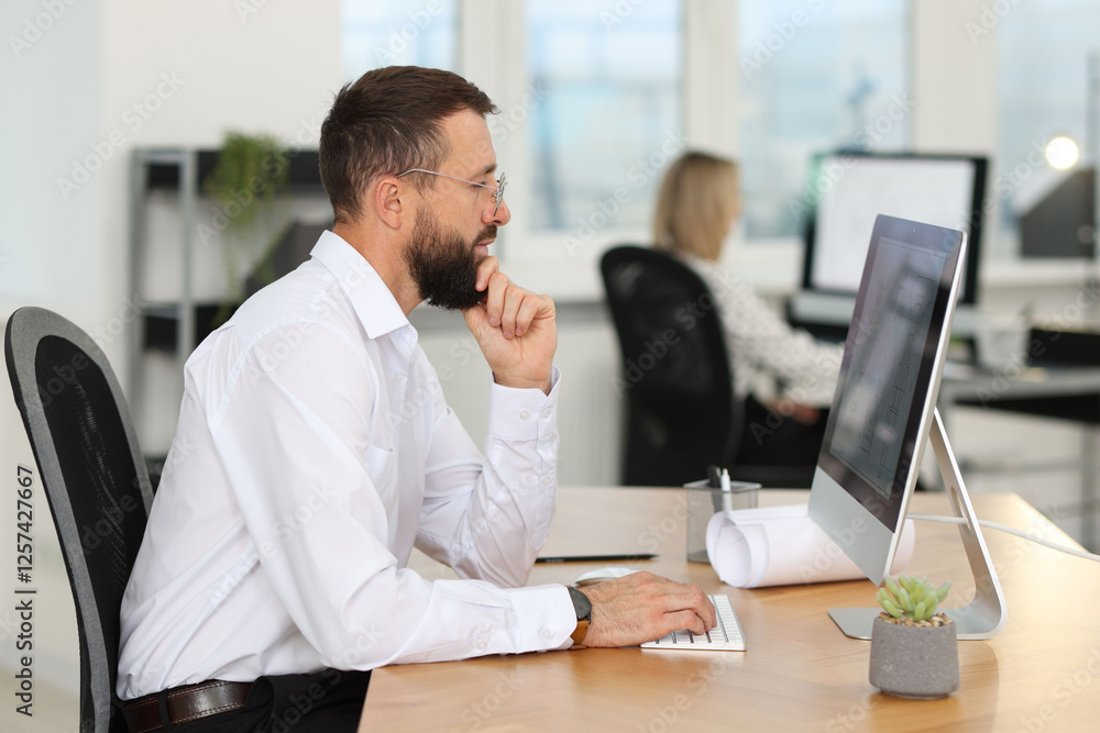 Poster technician making digital engineering drawing on computer at desk in office