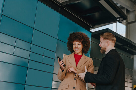 Businesswoman using smart phone with colleague near locker at parking