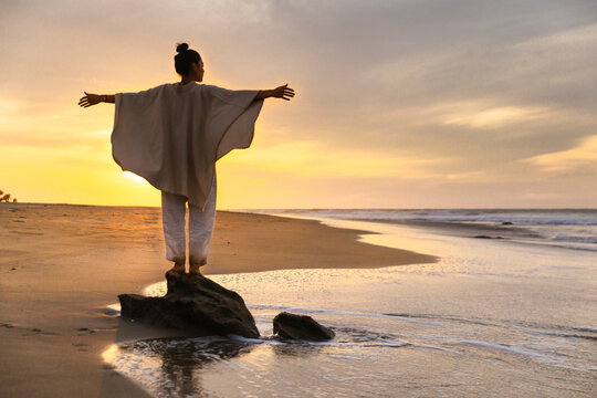 Carefree woman wearing poncho and standing on rock under cloudy sky