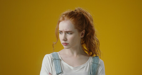 Close-up shot of a sad, scared, and angry red-haired teenage girl against a yellow background. She...
