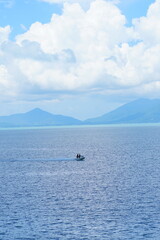 Fototapeta premium Serene tropical seascape with mountains under a bright blue sky and fluffy white clouds