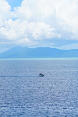 Fototapeta premium Serene tropical seascape with mountains under a bright blue sky and fluffy white clouds
