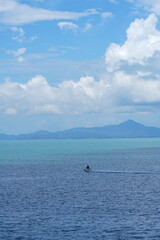 Obraz premium Serene tropical seascape with mountains under a bright blue sky and fluffy white clouds