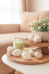 Easter eggs, candles and white ceramic rabbits on wooden table in interior of living room