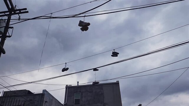 This intriguing slow-motion footage captures a curious urban scene: multiple pairs of shoes hanging from a power line, creating a unique visual against the city backdrop.