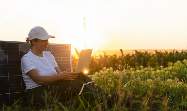 Woman farmer wearing white cap and t-shirt with laptop next to solar panel