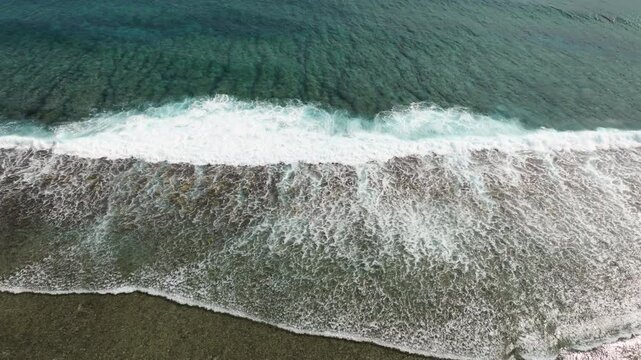 Aerial high angle descends on waves breaking on shallow fringing reef in ocean water