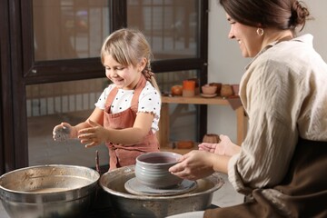 Hobby and craft. Smiling daughter with her mother making pottery indoors