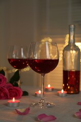 Romantic place setting with red wine and burning candles on table against blurred lights, closeup