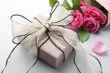 Gift box with beautiful bow and pink roses on light background, closeup