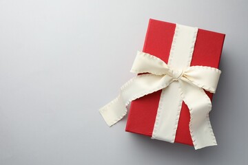 Gift box with beige bow on light grey background, top view. Space for text