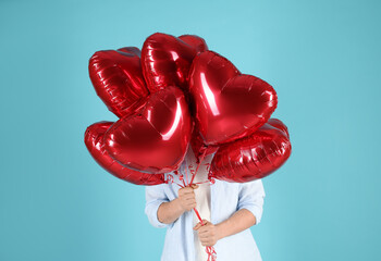 Man with red heart-shaped balloons on light blue background, closeup. Happy Valentine's Day