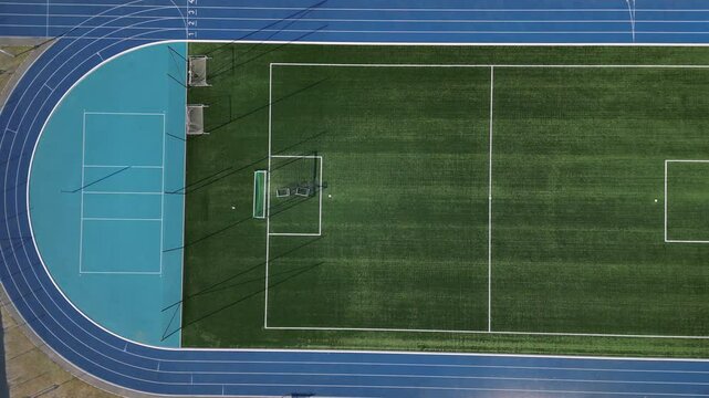 sports stadium with a running track with several lanes. inside oval there is a small football field for netball and handball with shield barriers. synthetic turf. view from top, all weather, rubber, 