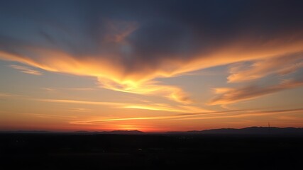 Fototapeta premium Breathtaking sunset painting the sky with vibrant shades of orange over a silhouetted landscape.