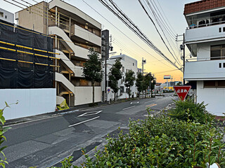 sunset street cityscape in in Nagoya, Japan - apartment buildings, construction, road, street signs, telephone poles and utility wires, trees, sidewalk, plants and bushes, stop sign