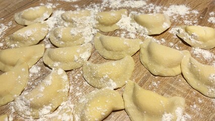 Freshly prepared homemade dumplings sprinkled with flour on a rustic wooden table, showcasing texture and craftsmanship, ready for boiling in a traditional cooking process.