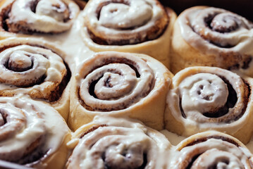 Fototapeta premium Freshly sweet baked cinnabon buns with cream chees sauce on baking paper. homemade rolls with Cinnabon cinnamon. Selective focus. French buns swirl, snail with glaze with cinnamon and cream
