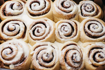 Fototapeta premium Freshly sweet baked cinnabon buns with cream chees sauce on baking paper. homemade rolls with Cinnabon cinnamon. Selective focus. French buns swirl, snail with glaze with cinnamon and cream