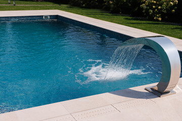 Luxury outdoor swimming pool with a modern stainless steel waterfall feature, creating a refreshing...