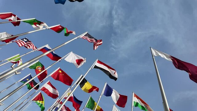 A collection of international flags waving on tall poles against a bright blue sky, symbolizing global unity and diversity.
