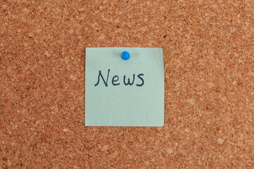 A light green sticky note with the handwritten word "News" attached to a corkboard with a blue push pin symbolizing announcements or updates