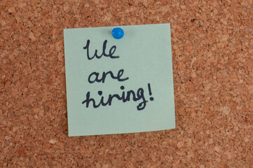 A corkboard features a light green sticky note announcing "We are hiring!" in handwritten black marker secured with a blue push pin
