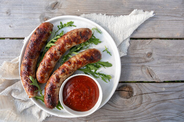 Three hot dogs are on a white plate with a red sauce