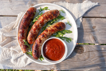 Three hot dogs are on a white plate with a red sauce
