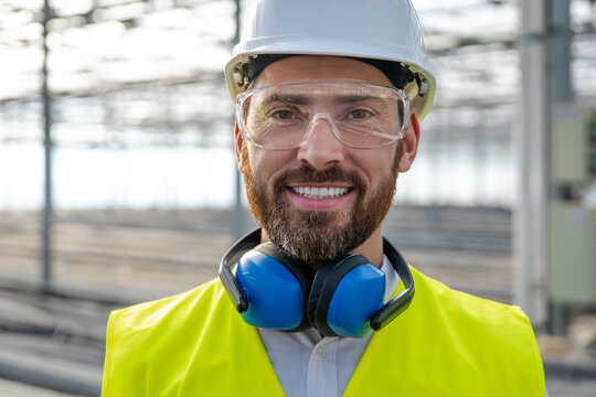 Smiling caucasian bearded engineer in protective glasses at the construction site