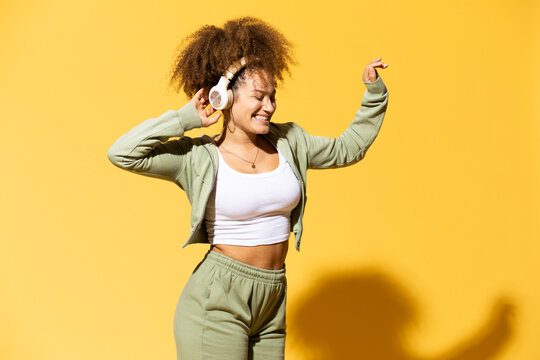 Curly haired woman with hand in hair standing in front of yellow background