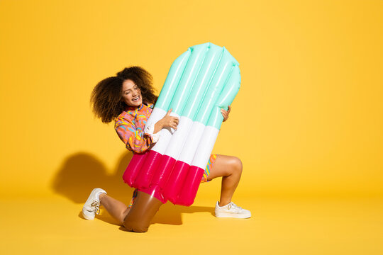 Playful woman having fun with air mattress in front of a yellow background
