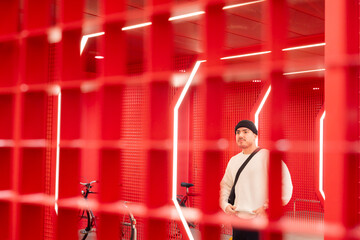 A stylish young man standing in a futuristic red-lit space with geometric design. Modern urban...